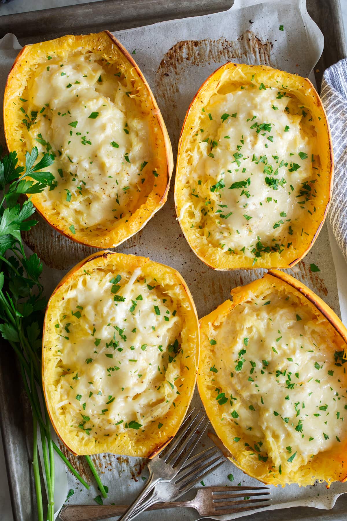 Overhead image of four spaghetti squash filled with cheese, they are resting on a parchment paper lined baking sheet.