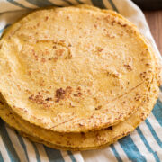 Stack of homemade corn tortillas on a blue striped kitchen towel.