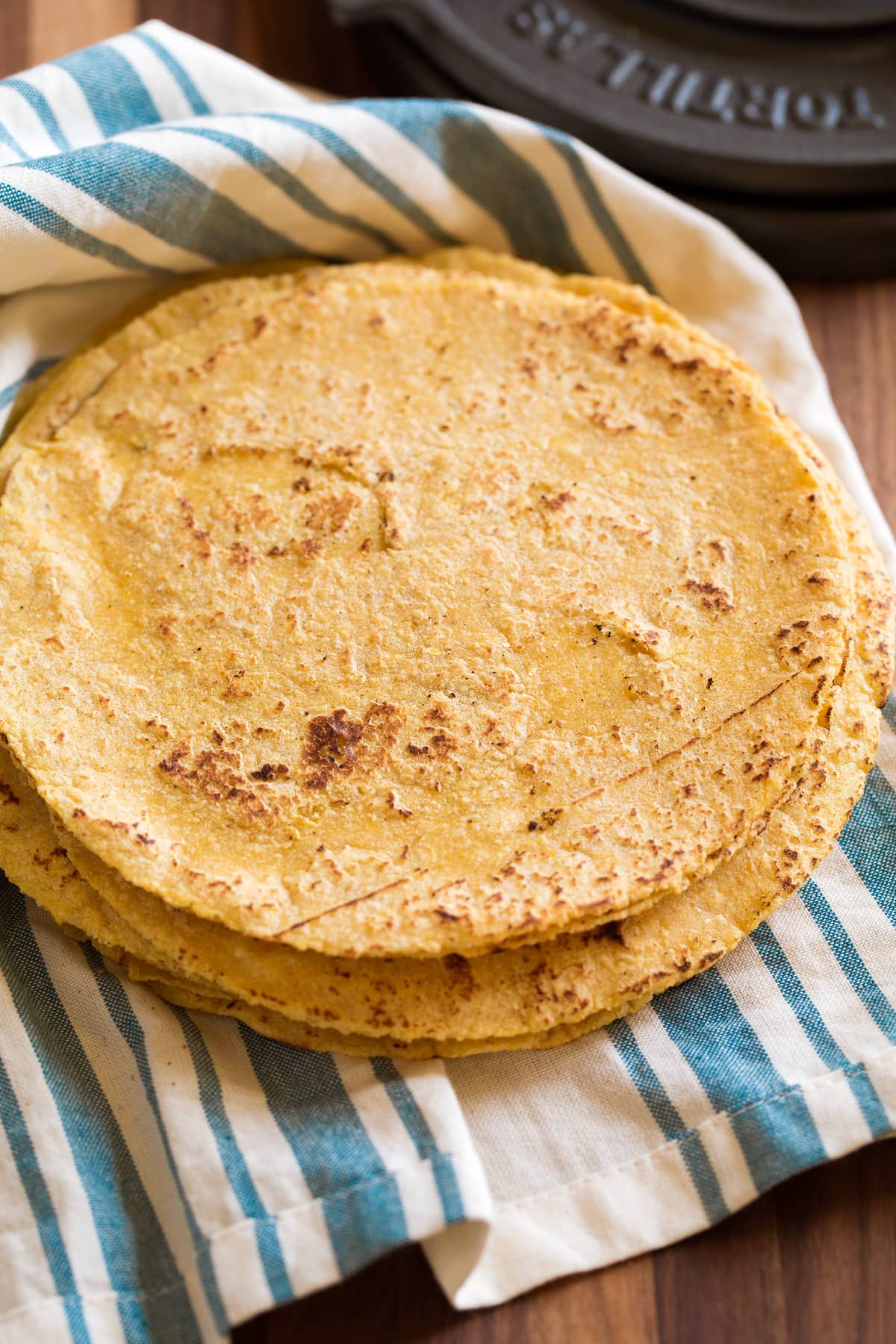 Stack of homemade corn tortillas on a blue striped kitchen towel.