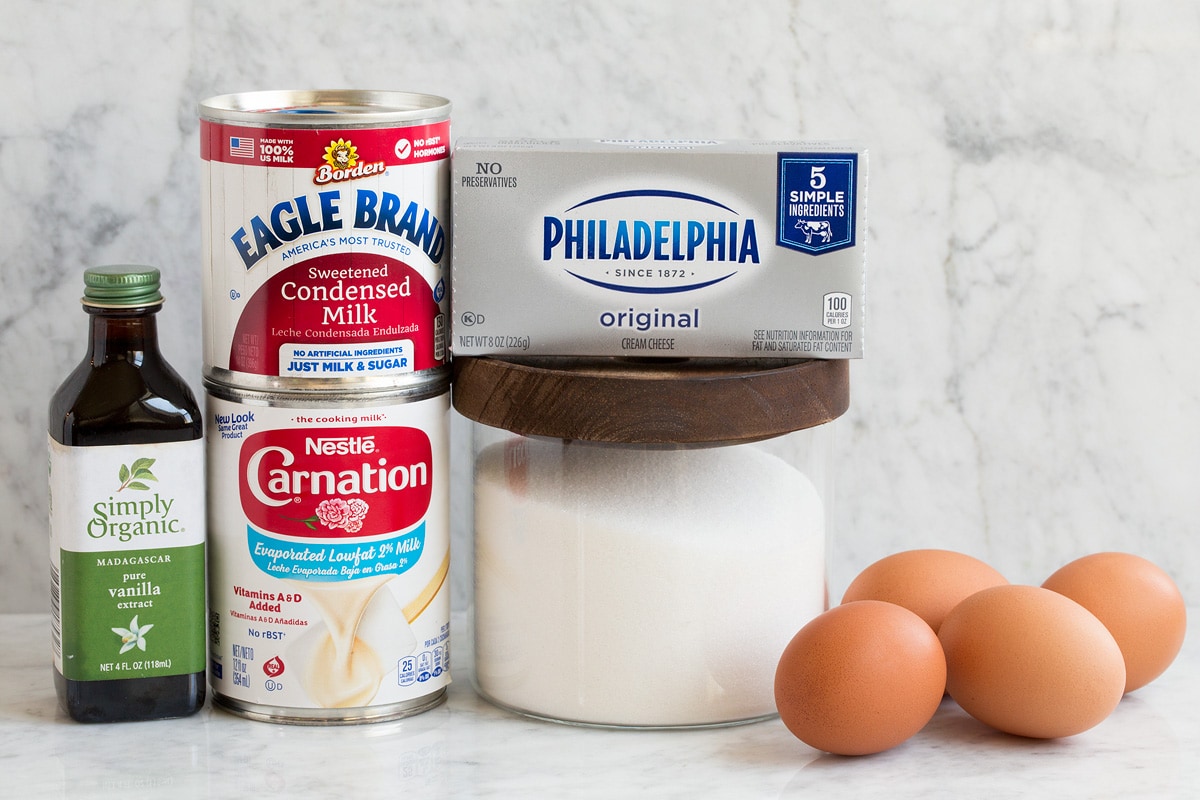 Image of ingredients used to make flan. Shows evaporated milk, sweetened condensed milk, granulated sugar, vanilla, eggs and cream cheese.