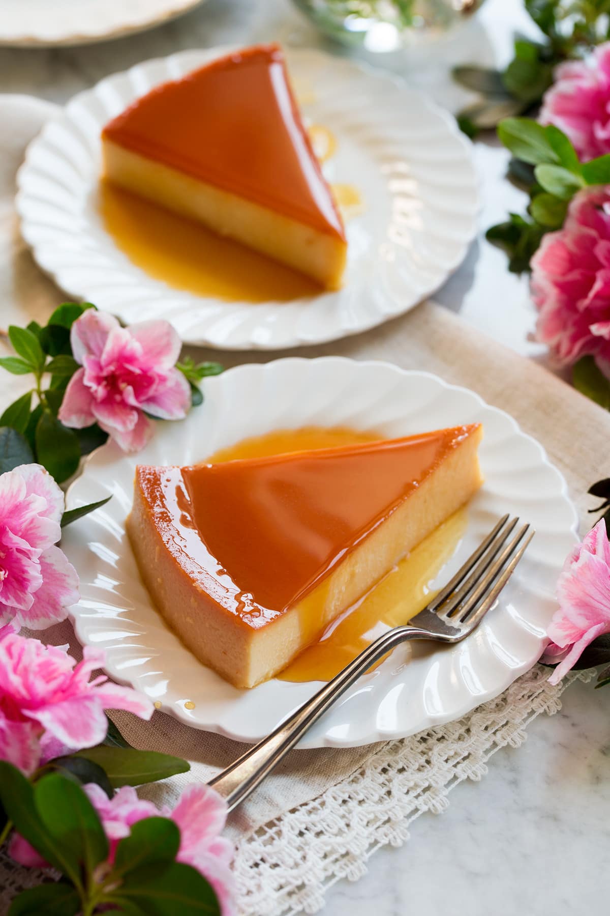 Image of two slices of flan on white scalloped plates with flowers around the sides.
