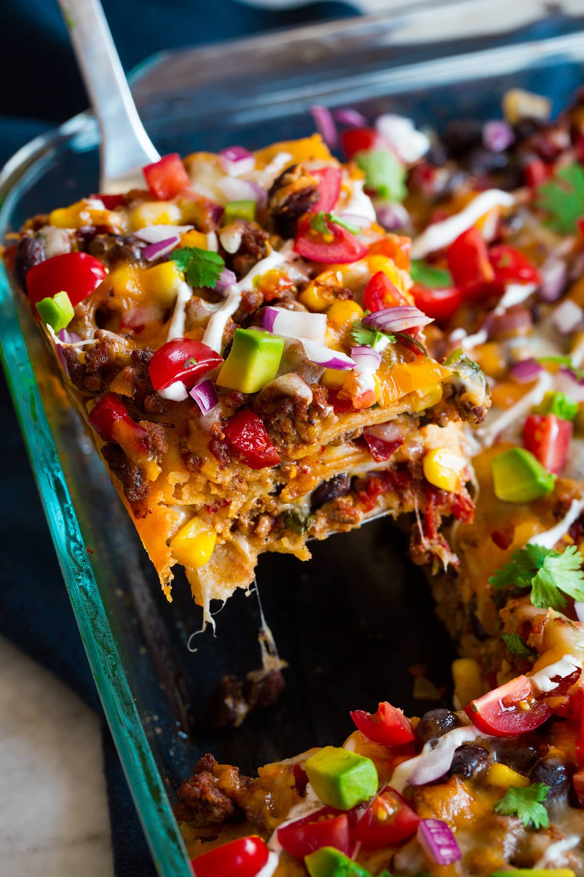 Close up image of slice of layered taco casserole being removed from baking dish.