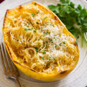 Roasted spaghetti squash half on a white serving plate. Squash it topped with browned butter, parmesan and parsley.