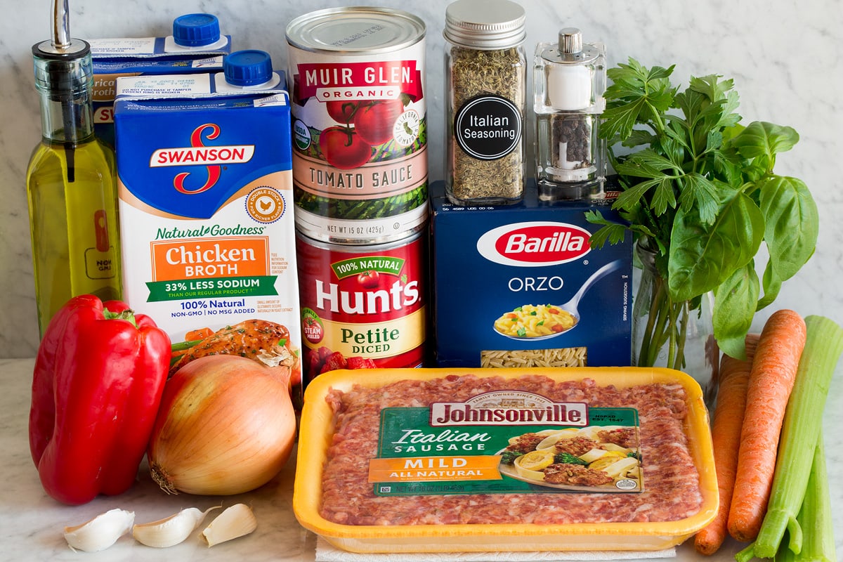 Image of ingredients used to make Italian sausage and orzo soup. Includes mild Italian sausage, orzo, carrots, celery, basil, parsley, Italian seasoning, salt and pepper, tomato sauce, diced tomatoes, chicken broth, yellow onion, bell pepper, olive oil and garlic.