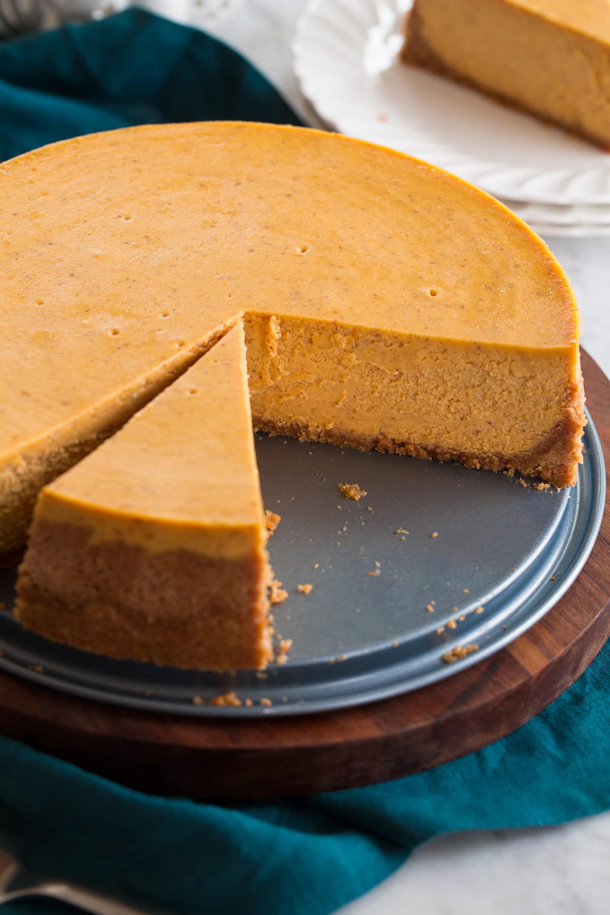 Nearly whole pumpkin cheesecake shown on a platter with a slice cut.
