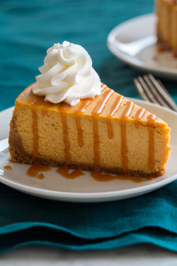Close up image of slice of pumpkin cheesecake that is topped with caramel sauce and whipped cream.