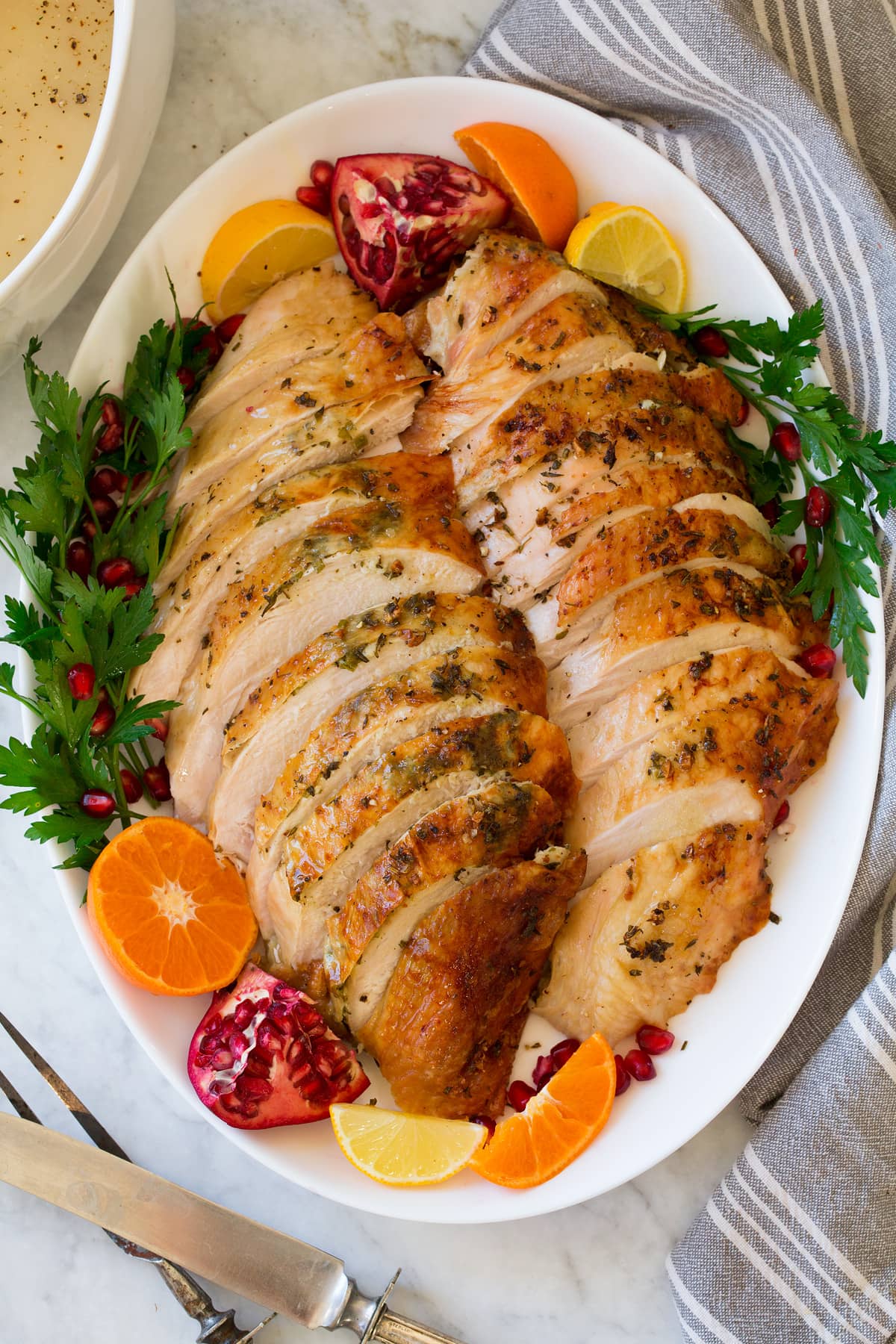Overhead image of sliced Roast Turkey Breast on a white oval platter with decorative fruit and herbs.