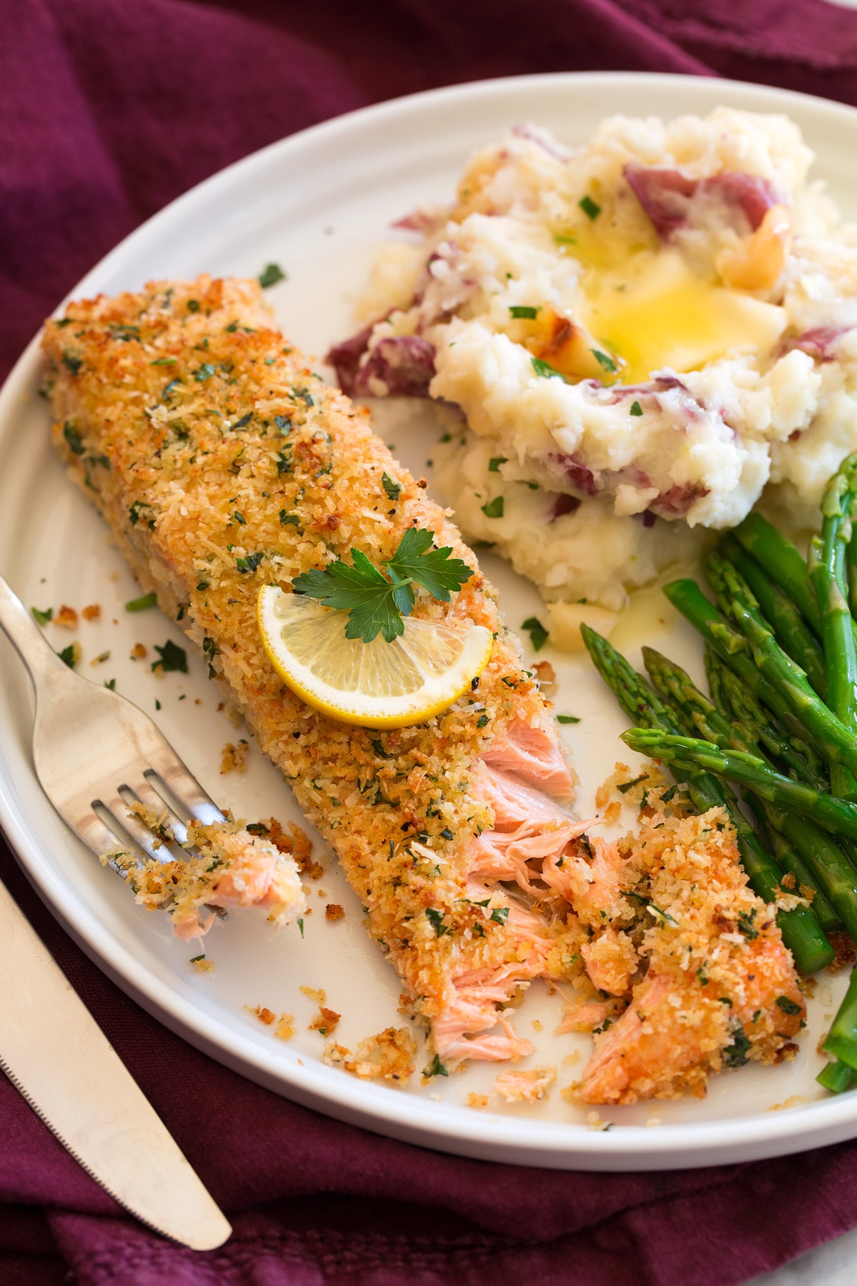 Baked salmon with parmesan and panko breadcrumb coating shown served on a plater with asparagus and garlic mashed potatoes. 