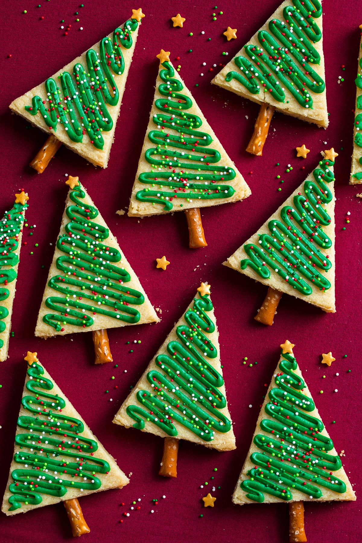Christmas Tree Cookies Triangular decorated Christmas tree cookies shown on a red surface.