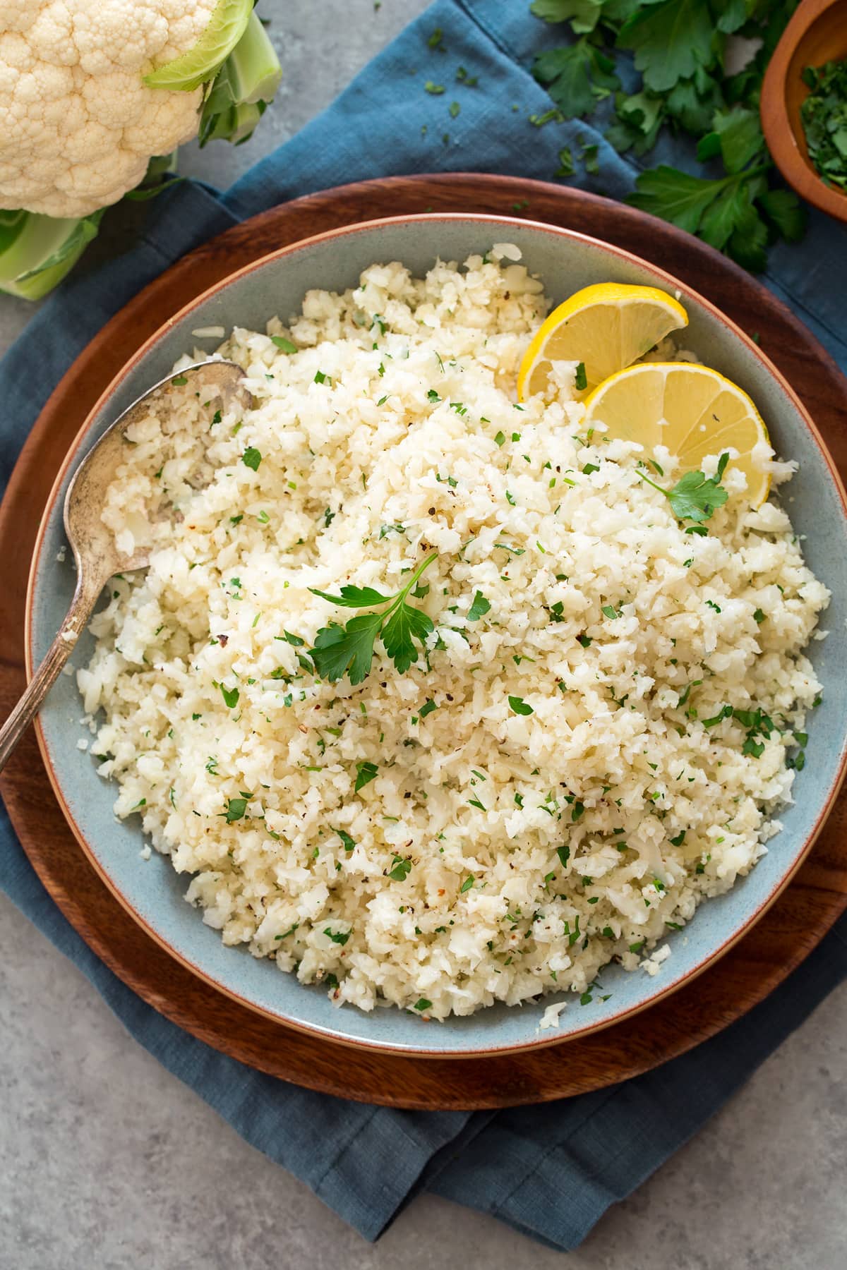 Cauliflower Rice Overhead photo of cauliflower rice in a blue bowl set over a wooden plate.