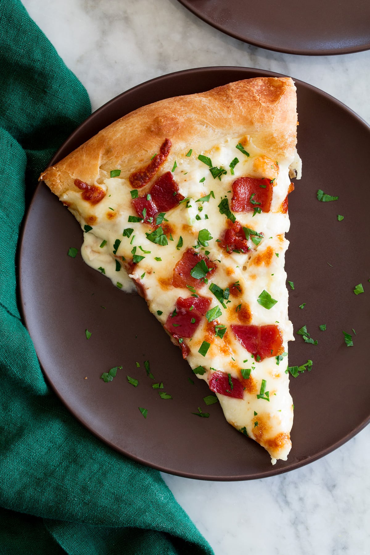 Slice of chicken Alfredo pizza topped with bacon set on a brown plate over a marble surface.