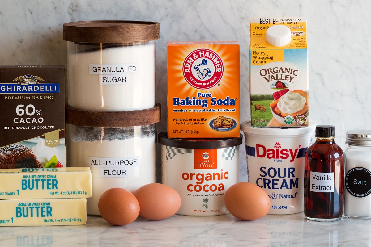 Photo of ingredients used for chocolate bundt cake. Includes flour, sugar, butter, chocolate, eggs, cocoa powder, baking soda, cream, sour cream, vanilla and salt.
