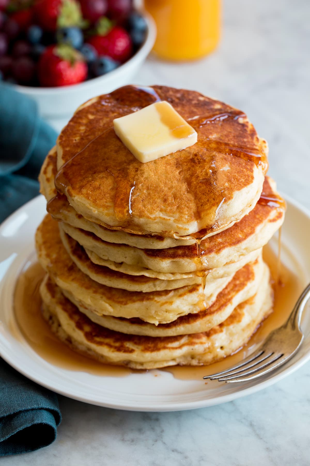 Stack of homemade pancakes on a white plate. Pancakes are topped with maple syrup and butter.