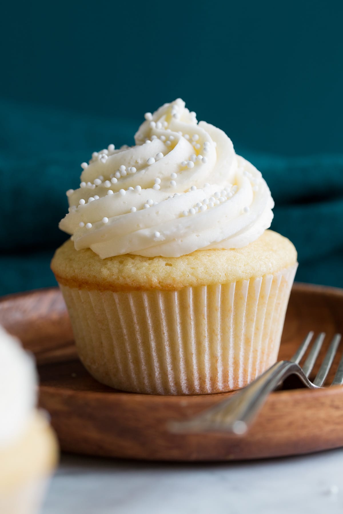 Close up photo of single vanilla cupcakes on a wooden dessert plate on a marble surface with a blue backdrop.