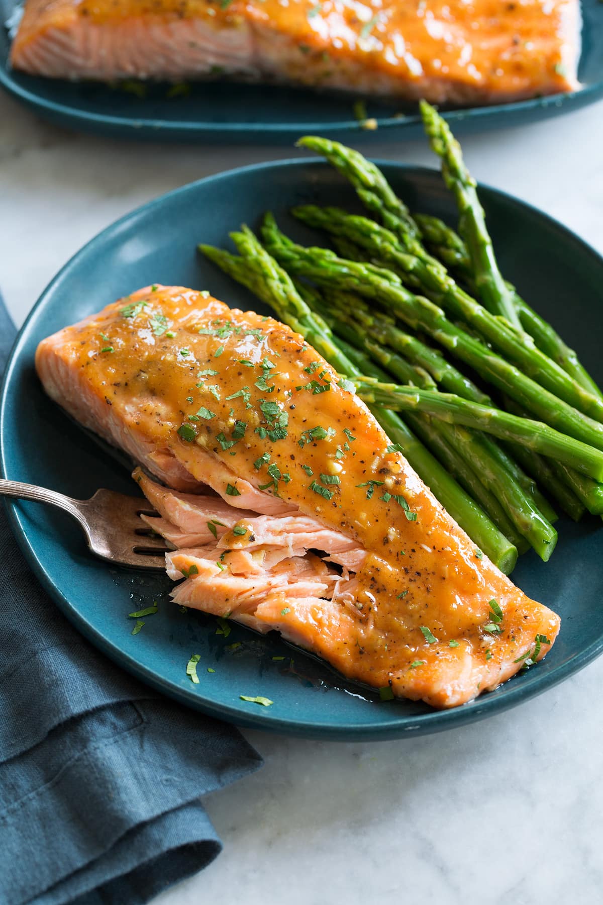 Brown Sugar Glazed Salmon Photo of brown sugar salmon with serving suggestion of steamed asparagus. Served on a blue plate with a blue cloth to the side.