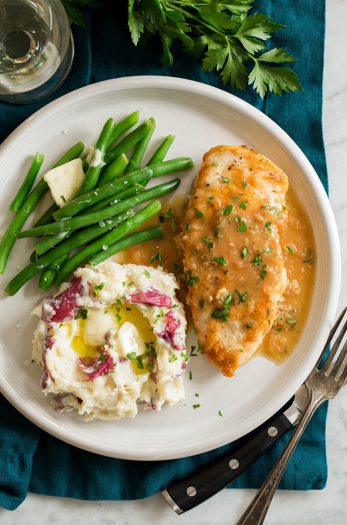 Chicken in white wine sauce shown served with green beans and buttered mashed potatoes on a white dinner plate.