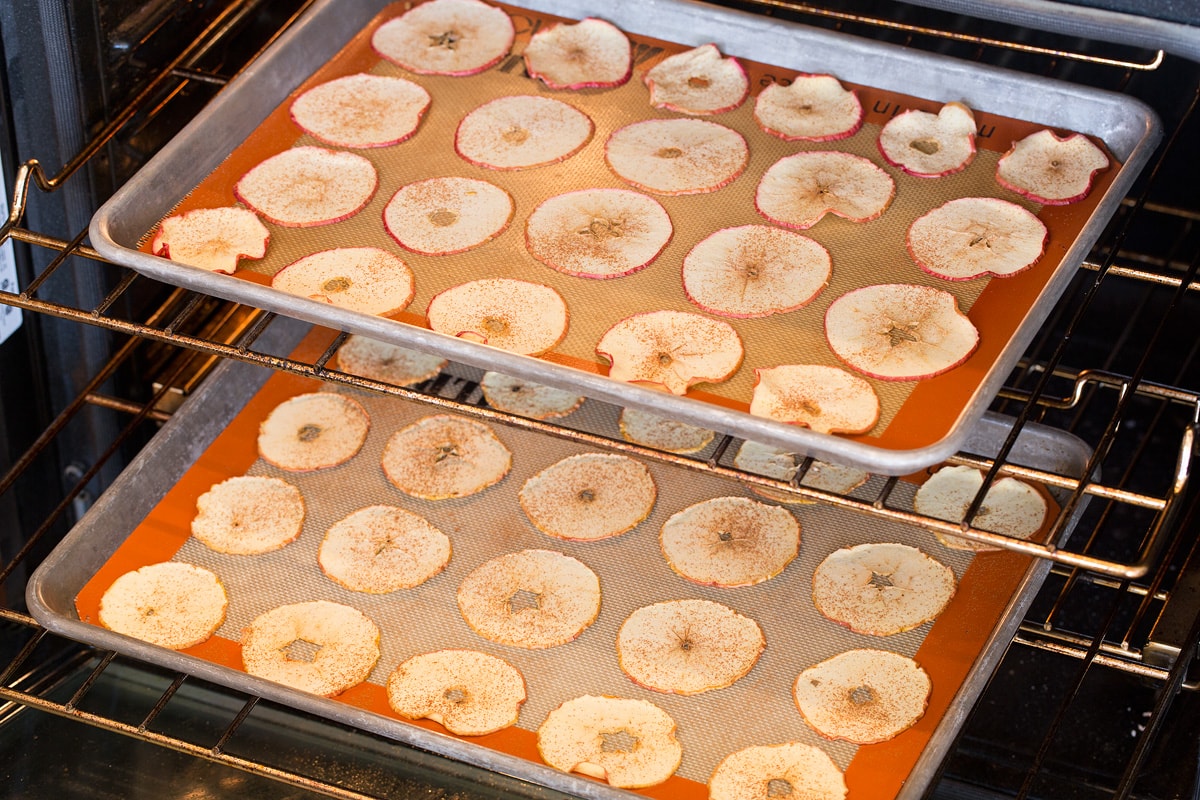 Baked Apple Chips Apple slices being baked in an oven on two baking sheets set on two oven racks.