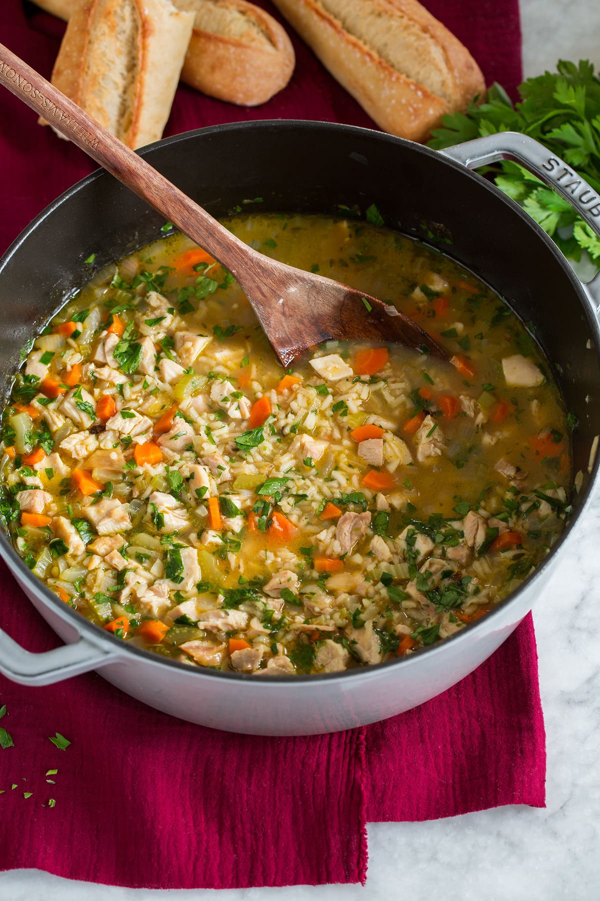 Pot of chicken and rice soup with a wooden ladle. Baguette bread is shown in the background.