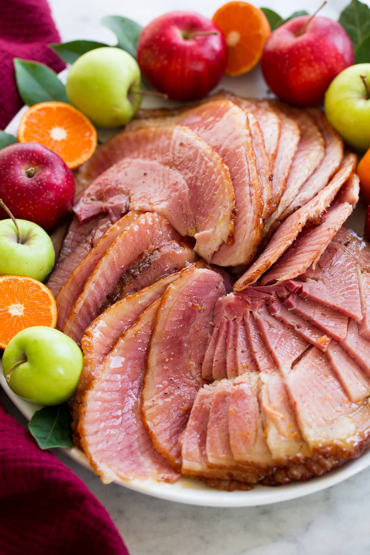 Crockpot Ham Spiral sliced ham that was cooked in a slow cooker shown on an oval white serving platter close up with decorative fruit and herbs to the sides.
