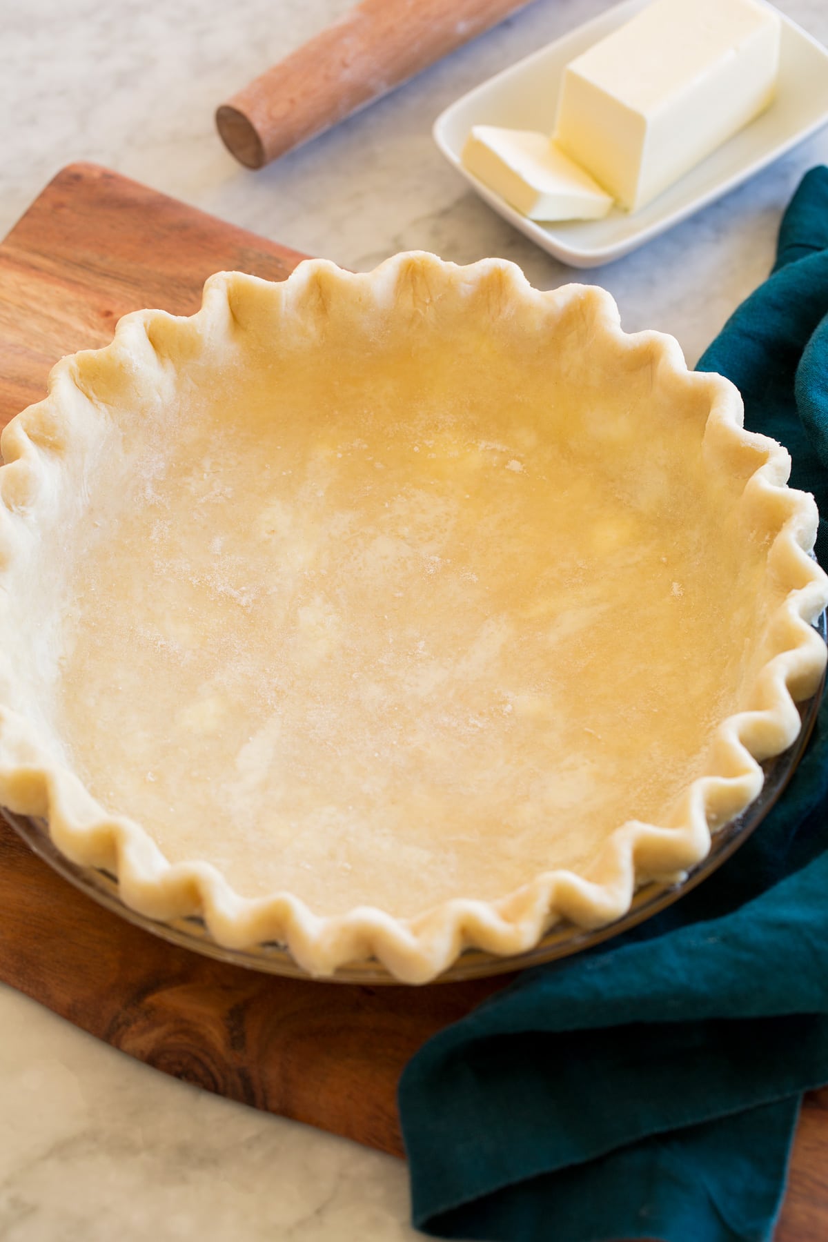 Homemade Pie Crust Pie Crust shown before baking in a glass pie pan set on a wooden platter.