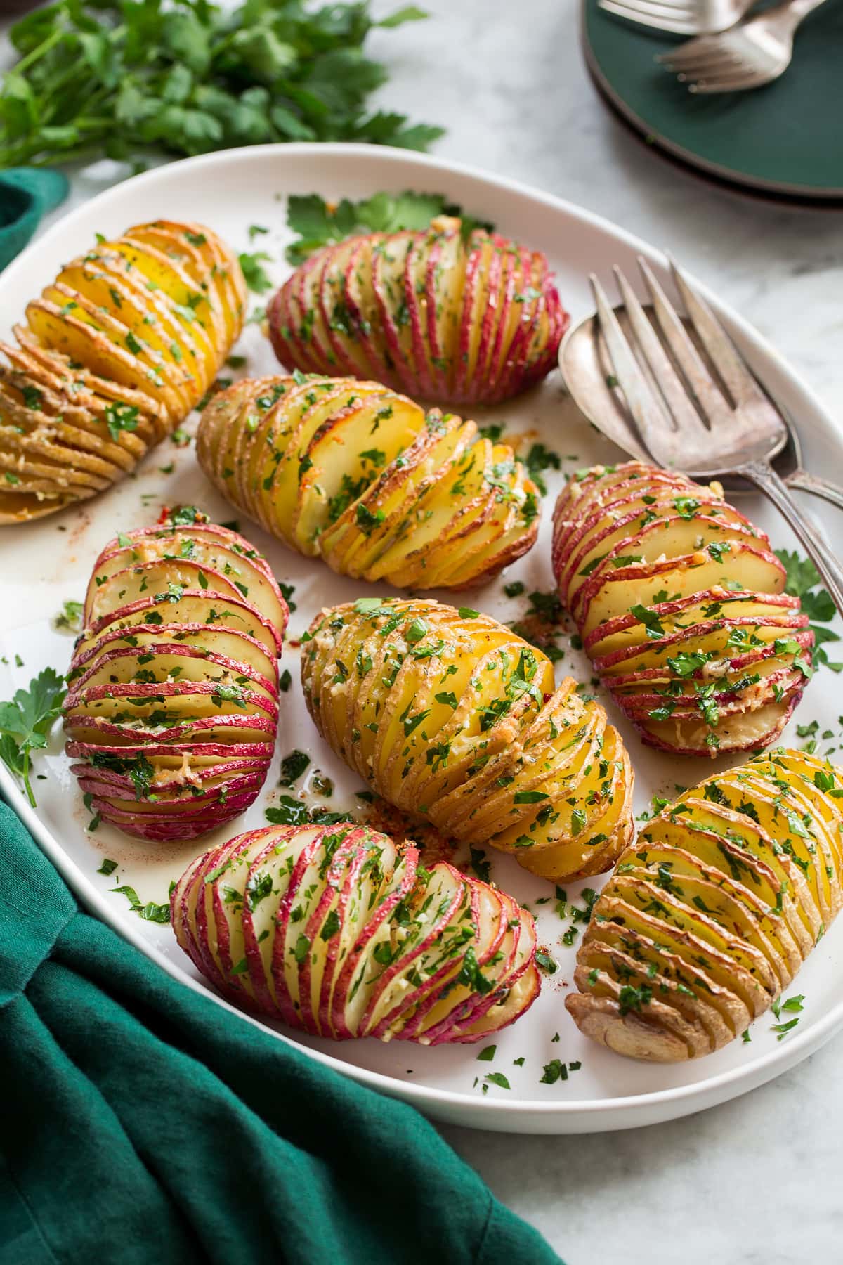 Hasselback Potatoes Hasselback potatoes on a serving platter on a marble surface with a green cloth.