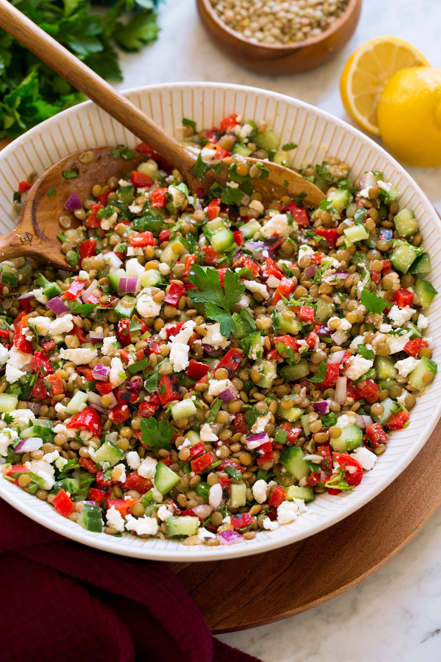 Lentil salad shown in a white ceramic serving bowl. Made with green lentils, bell pepper, red onion, feta, cucumber and dressing.