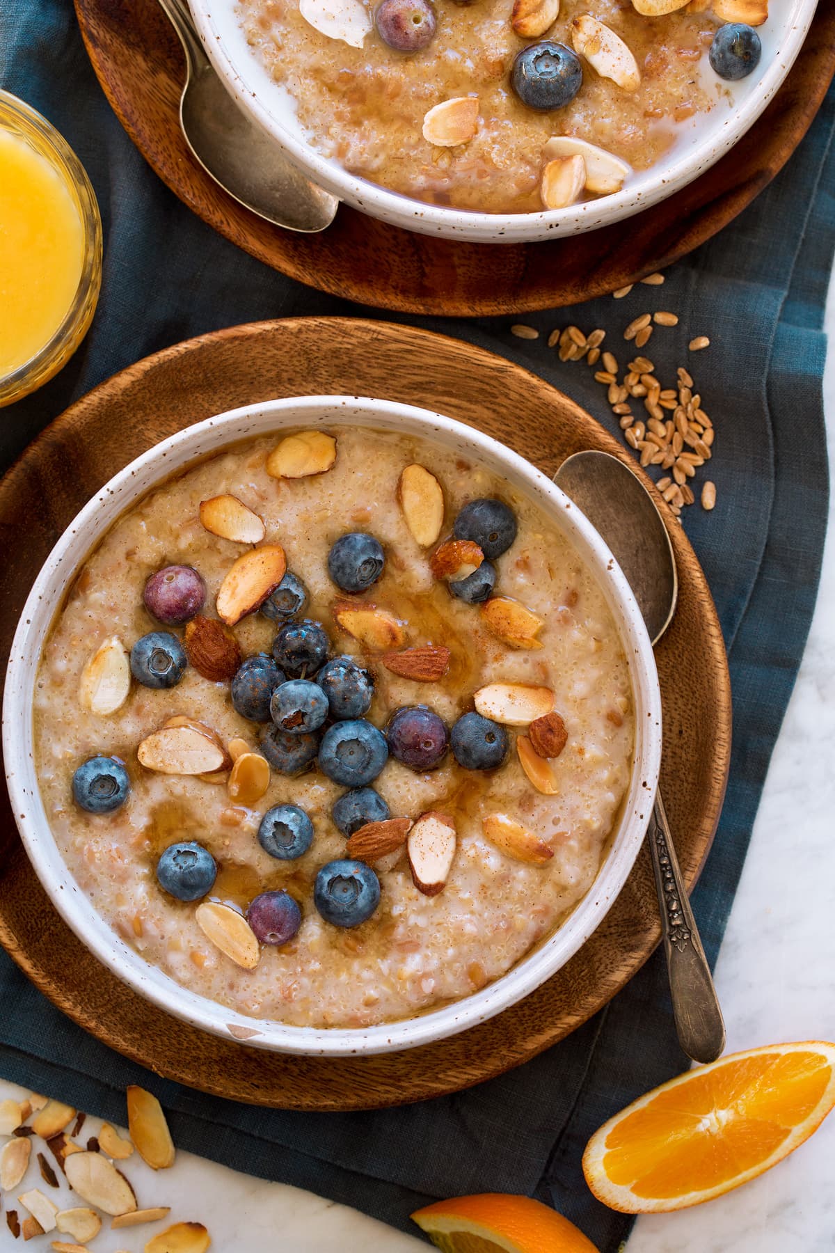 Multigrain Porridge Porridge shown in a white bowl over a wooden plate with dried grains to the side. It is shown served with orange juice.