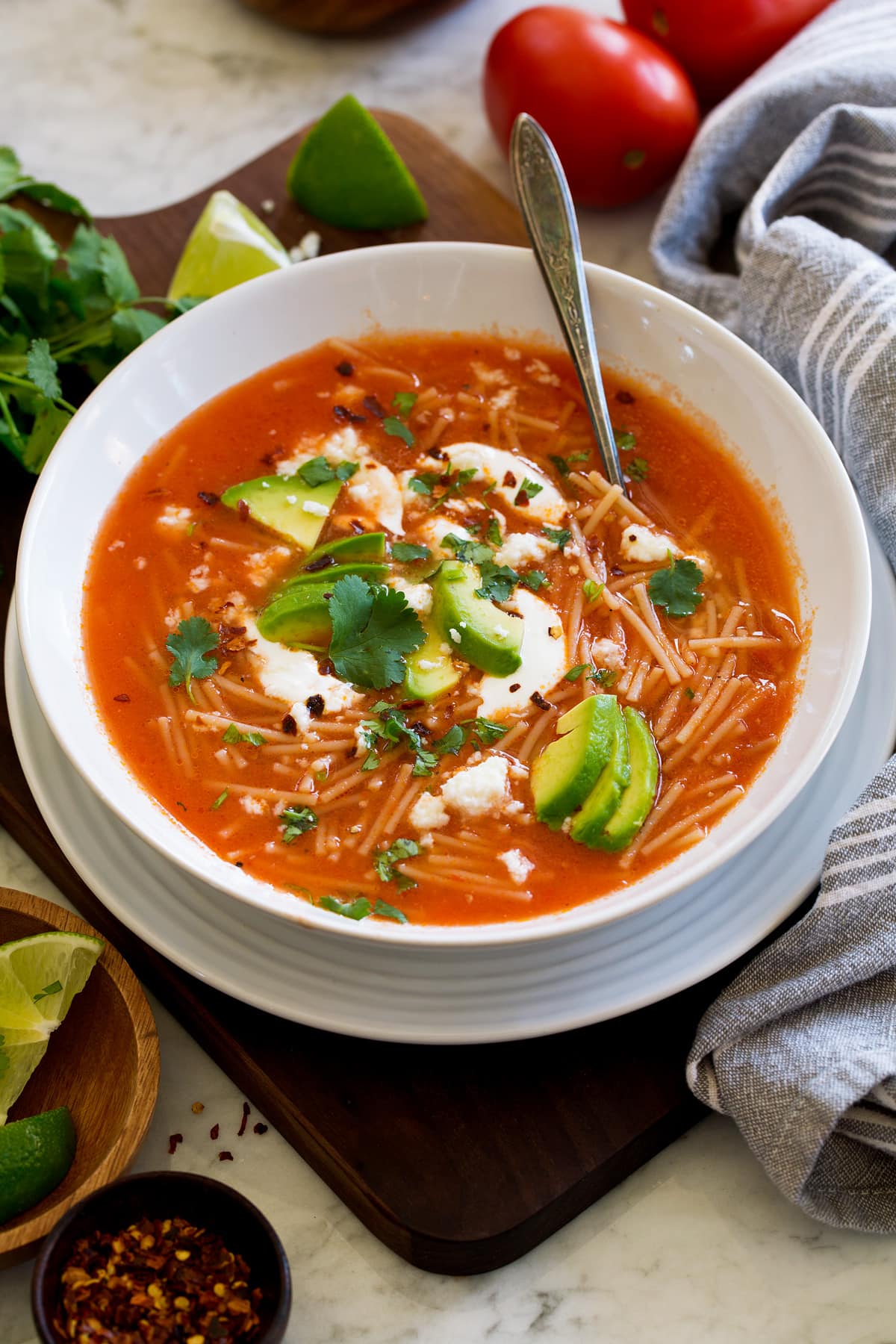Sopa de fideo in a white soup bowl. Shown topped with avocado, cilantro, mexican crema, and queso fresco.
