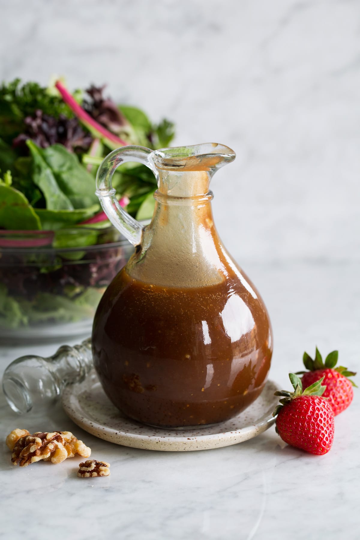 Balsamic vinaigrette in a glass salad dressing jar set over a small plate. A green salad is shown in the background.