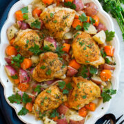 Braised chicken and vegetables on a white oval platter on a marble surface..