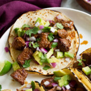 Single steak taco with avocado, cilantro and red onion shown close up.