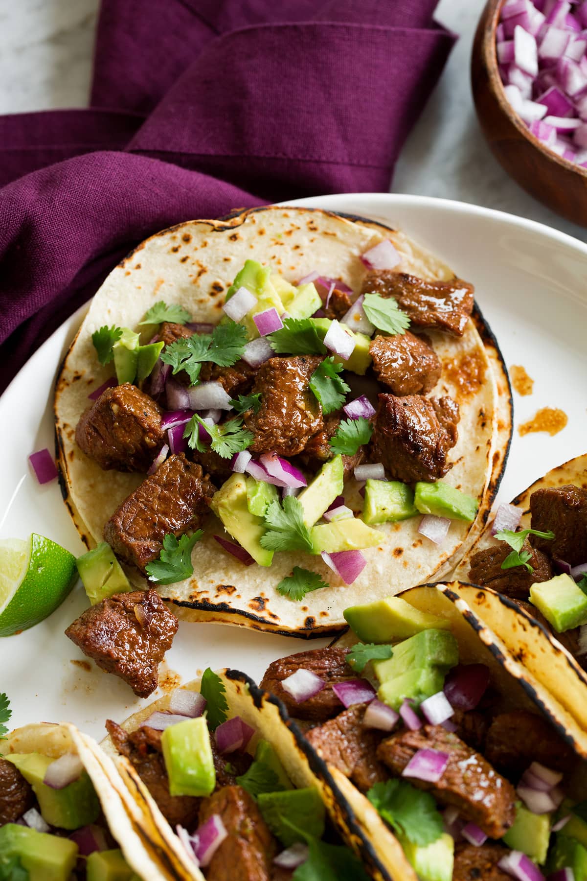 Single steak taco with avocado, cilantro and red onion shown close up.
