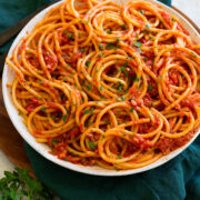 Bucatini with amatriciana sauce in a white serving bowl with parmesan cheese and parsley garnish.
