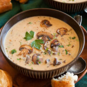 Single serving of cream of mushroom soup in a brown bowl garnished with sauteed mushrooms.