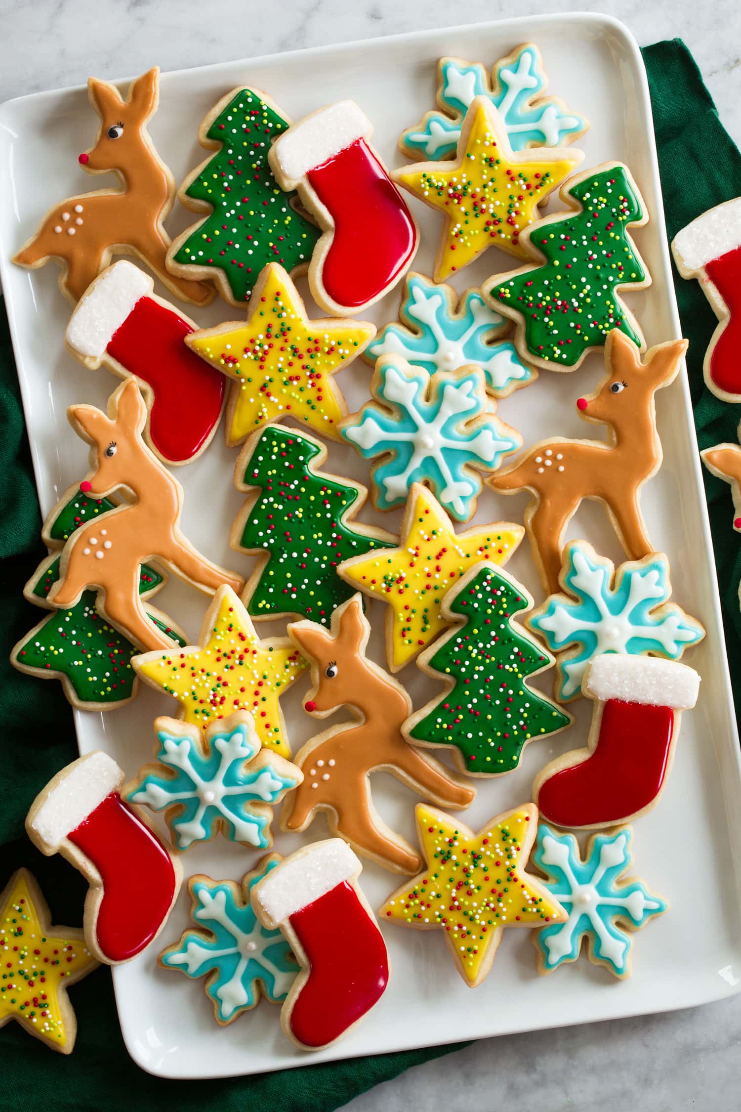 Sugar Cookie Icing Cut out Christmas sugar cookies decorated with easy icing. Shown on a white rectangular platter from overhead. There are dear shapes, trees, stars, snowflakes and stockings.
