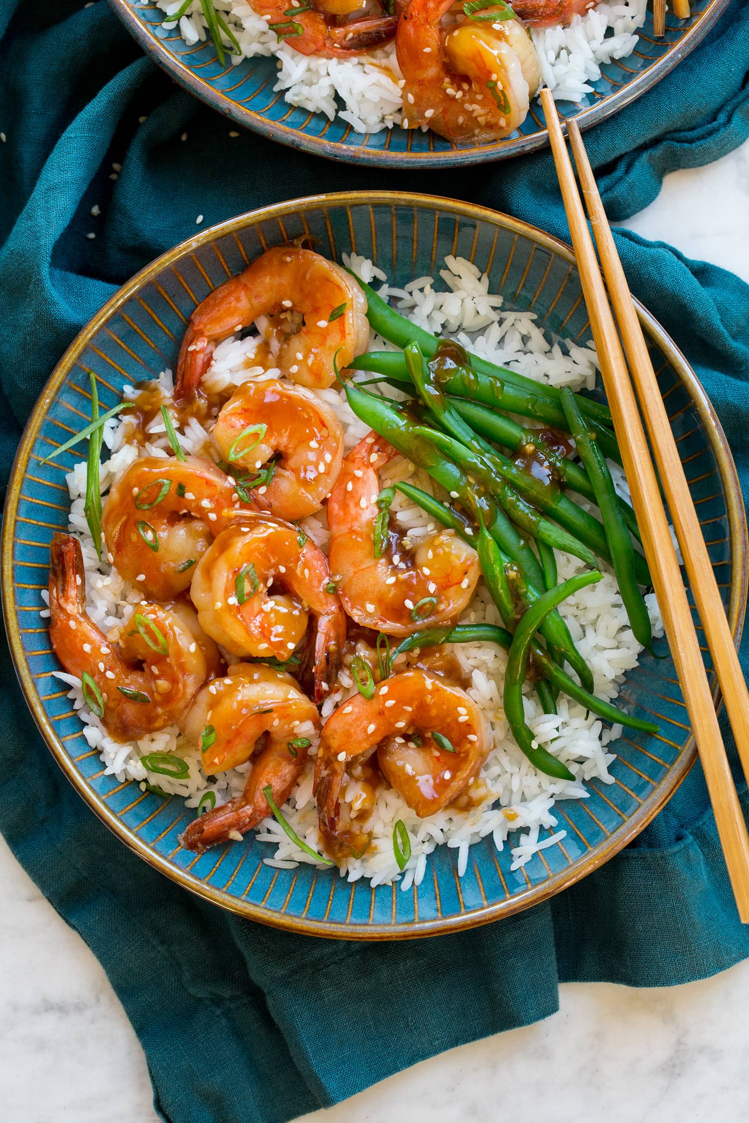 Teriyaki Shrimp Teriyaki shrimp in a blue bowl with rice, green beens and green onions. Shown with a blue cloth and chopsticks.