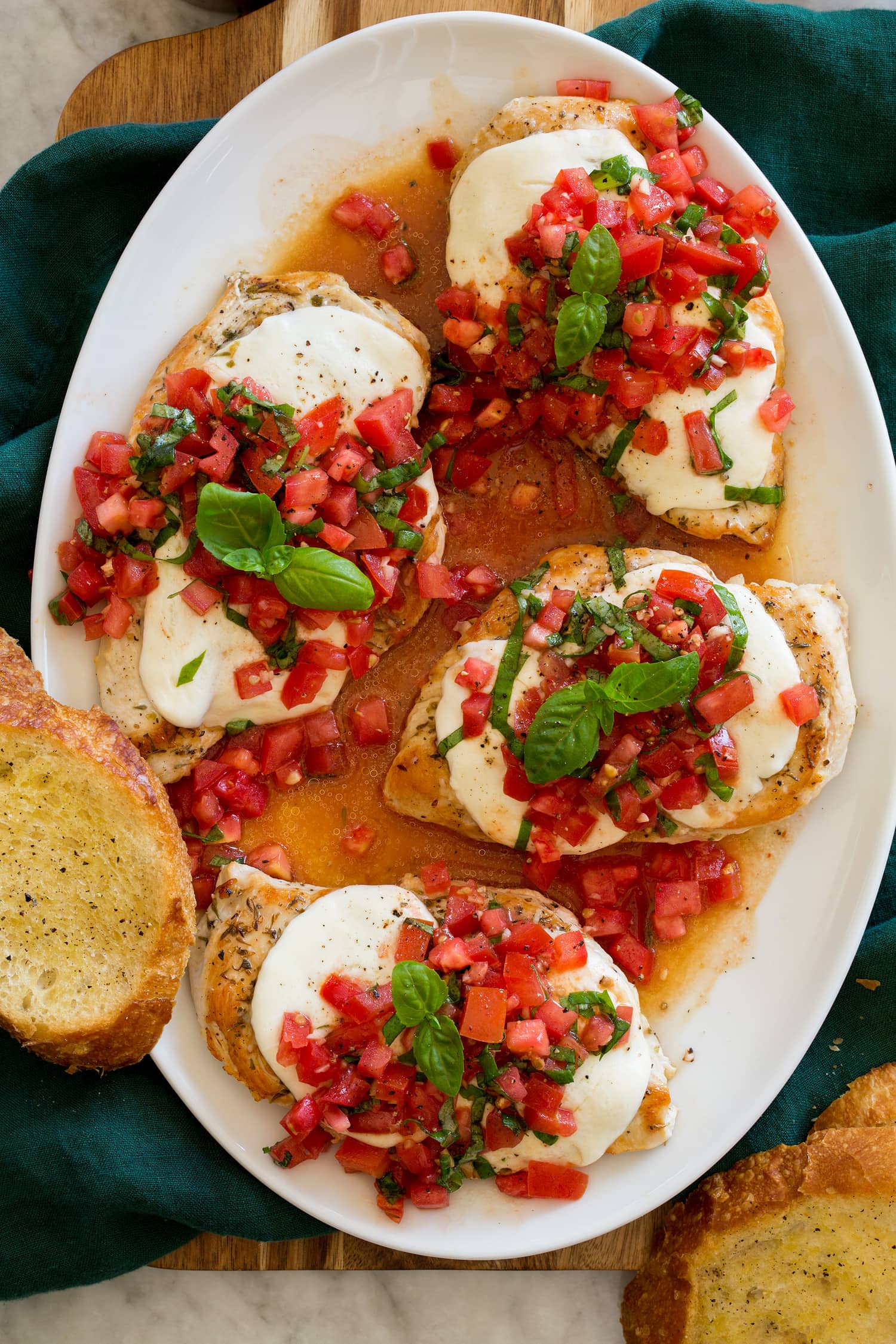 Bruschetta Chicken Overhead photo of four servings of bruschetta chicken on a white oval serving tray shown from above.