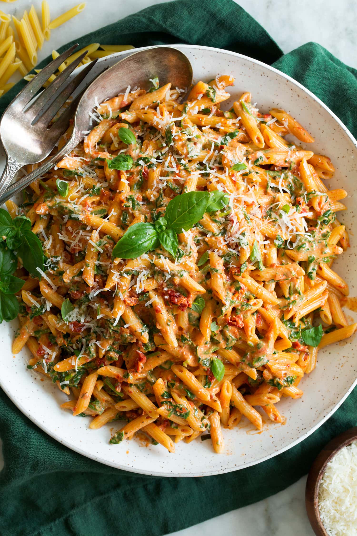 Sun Dried Tomato Pasta with creamy sauce shown in a white ceramic bowl over a green cloth.