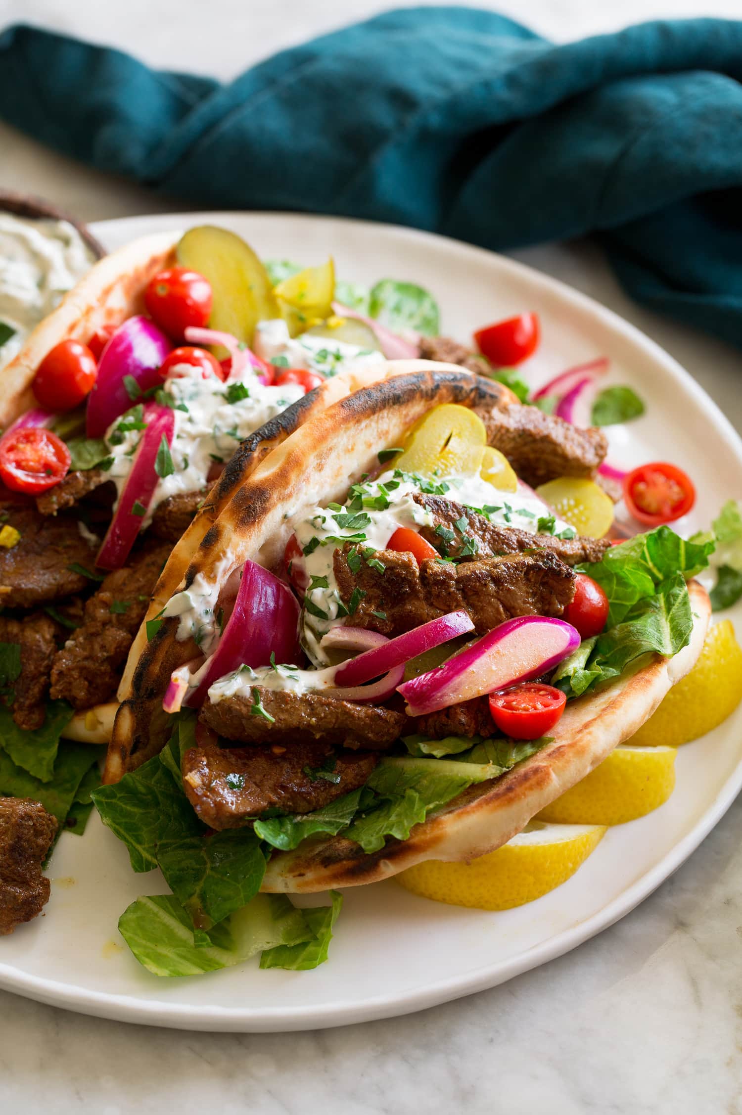 Beef Shawarma Beef shawarma shown in a pita with lettuce, tomatoes, red onion, pickles and a tahini yogurt sauce.