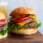 Hamburger shown on homemade bun with lettuce, cheddar, tomatoes and pickles.