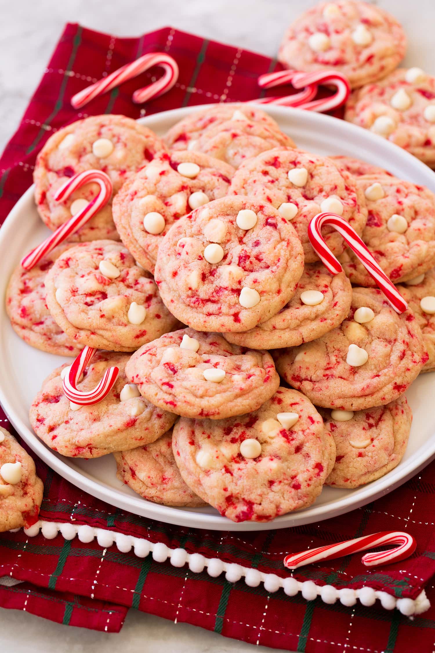 Peppermint white chocolate chip cookies stacked on a plate with candy canes decorating them.