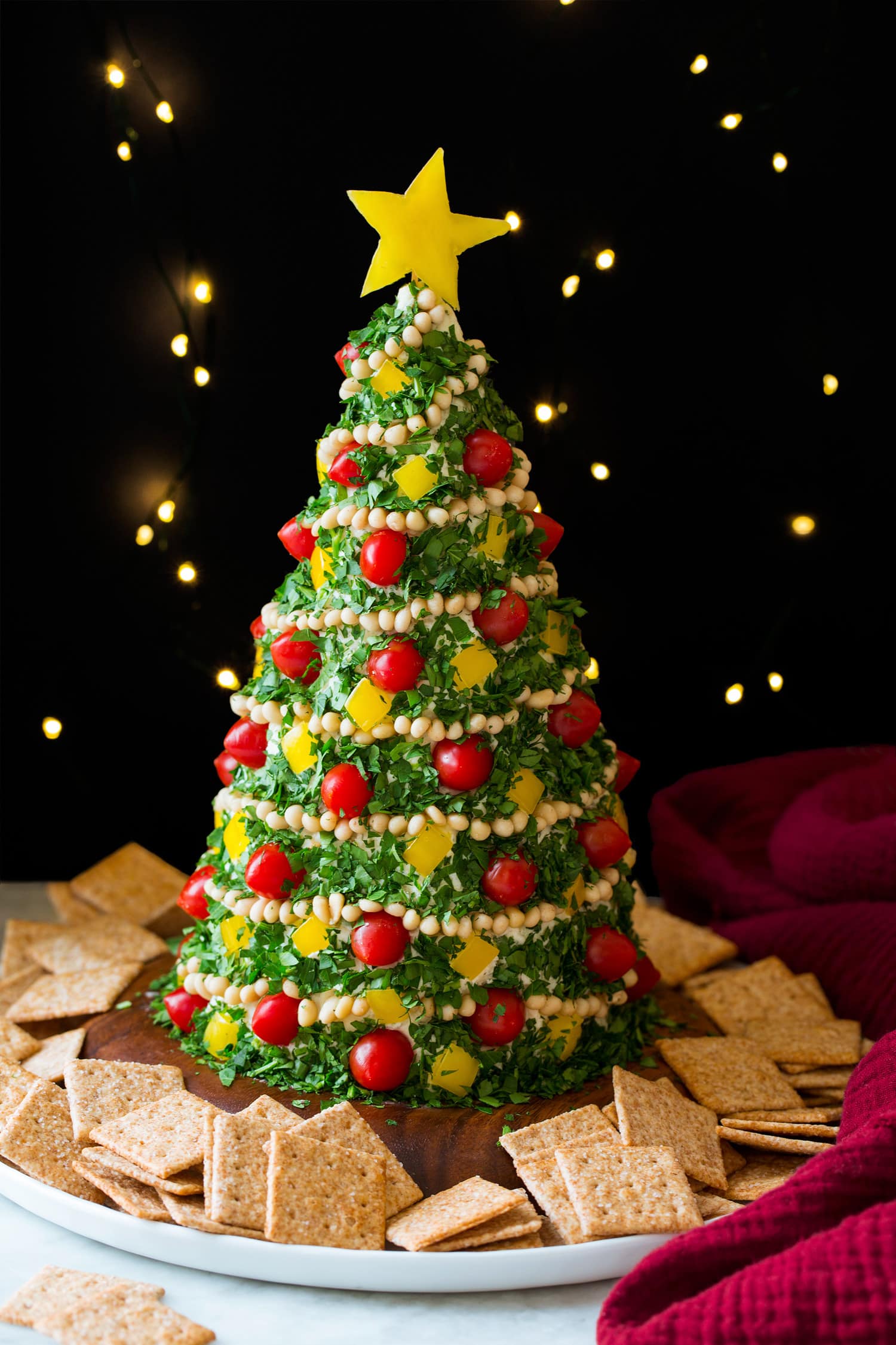 Christmas Tree Cheese Ball Christmas tree cheese ball with lights in the background and crackers around the tree.