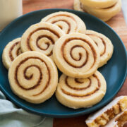 Cinnamon roll cookies piled on a blue plate on a wooden surface.