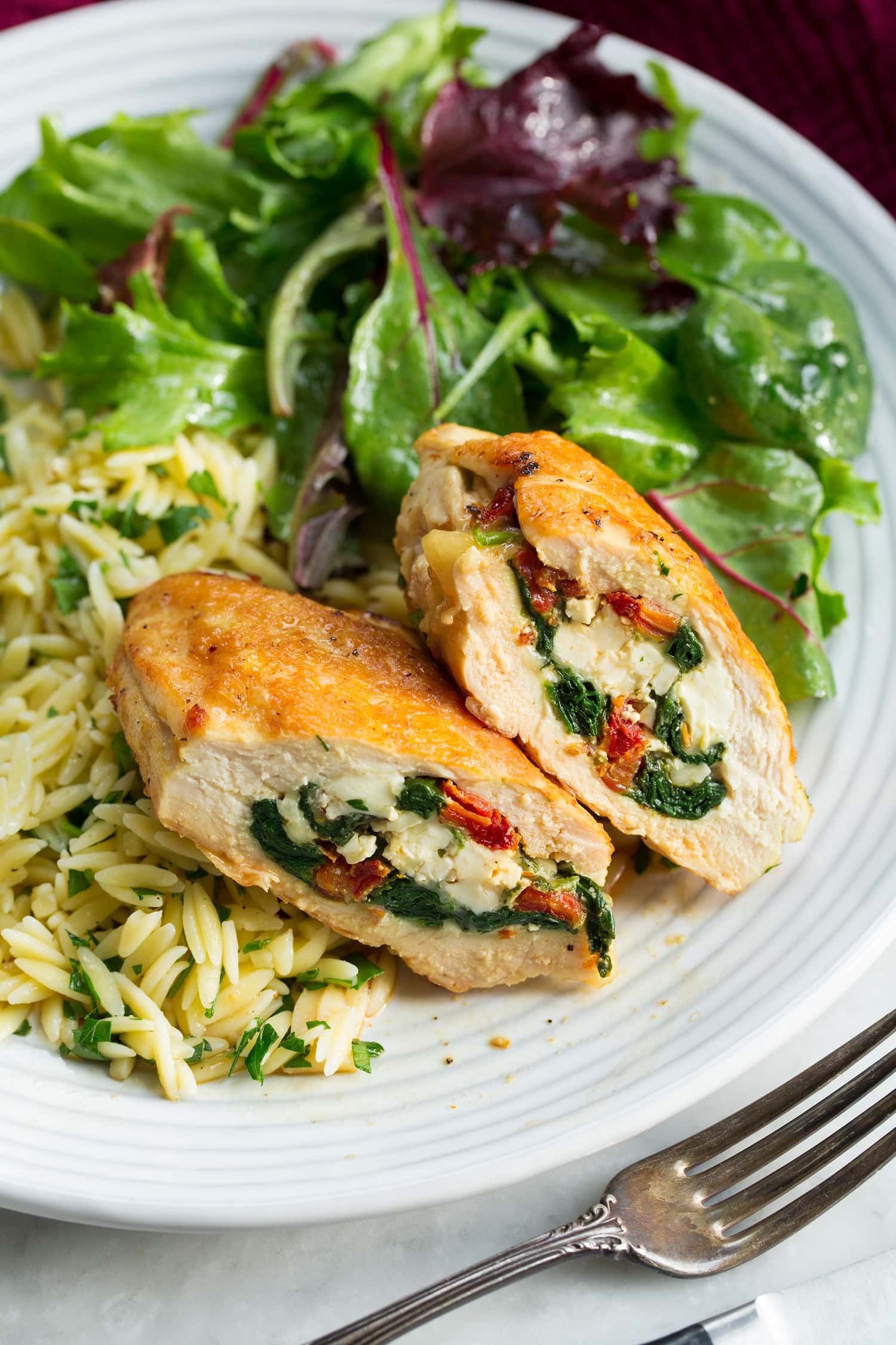 Stuffed Chicken Breasts Two sliced stuffed chicken breasts halves shown with serving suggestions of side salad and lemon orzo.