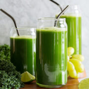Three servings of green juices made with different greens including spinach, romaine lettuce and kale. Also includes cucumber, grapes, apples, celery, broccoli, lime and ginger.