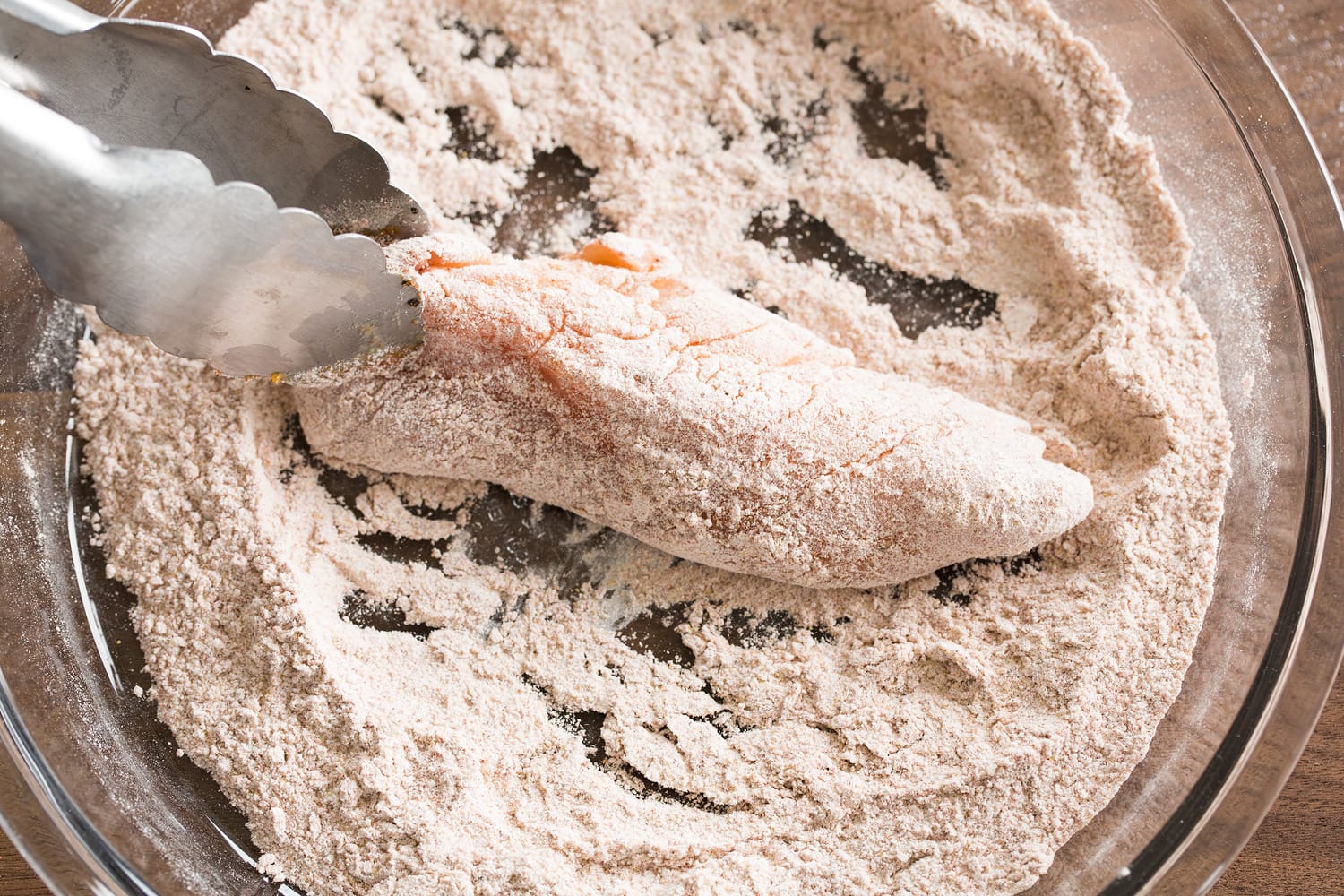 Hot Honey Chicken Coating chicken piece in flour mixture.