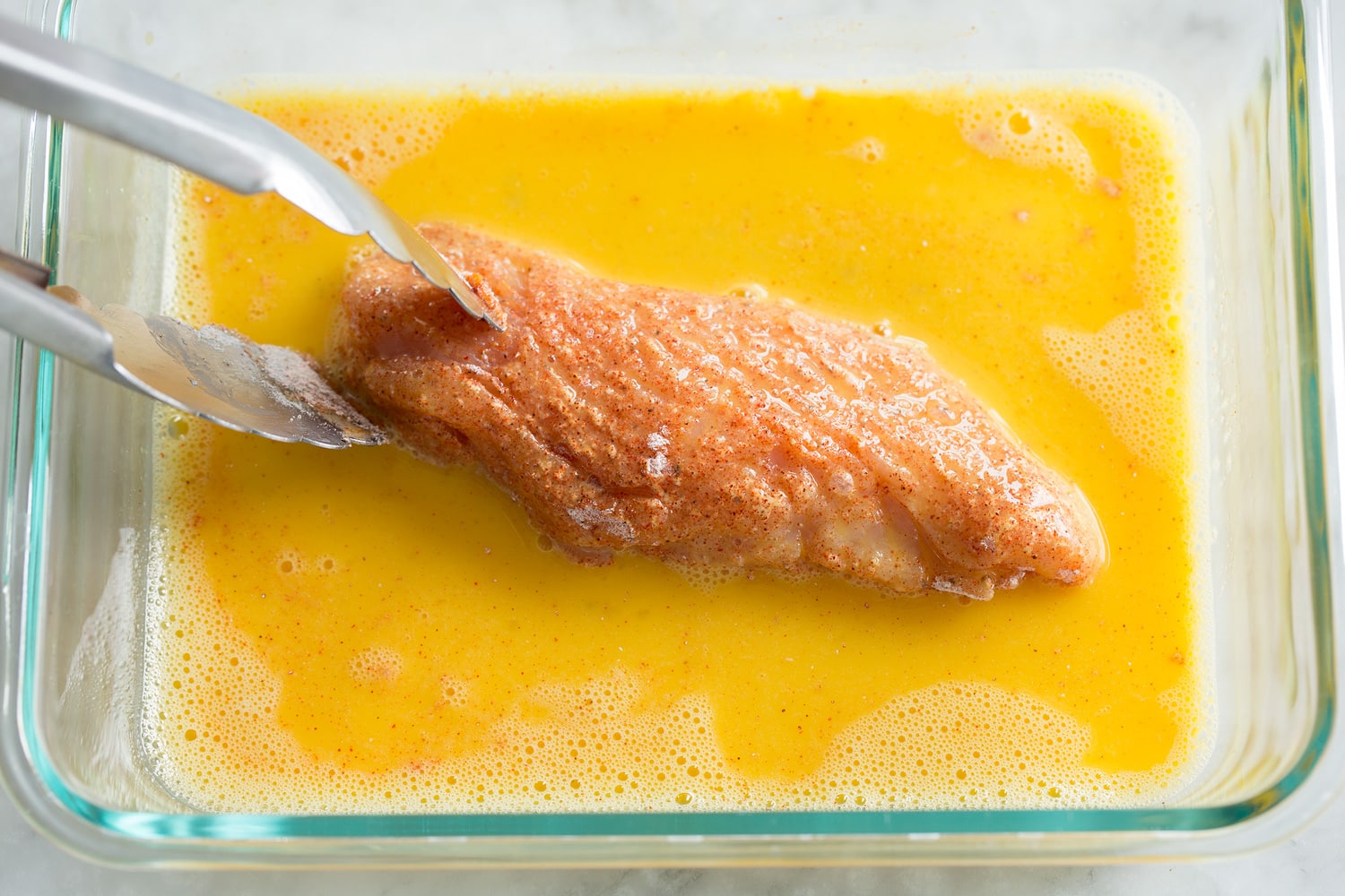 Hot Honey Chicken Coating chicken piece in egg mixture.