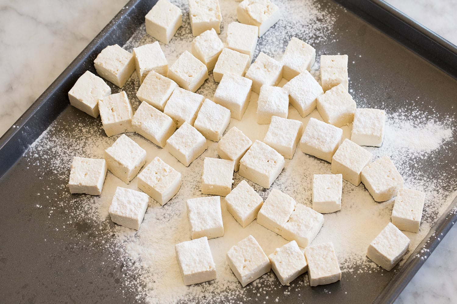 Tofu cubes being tossed in cornstarch.