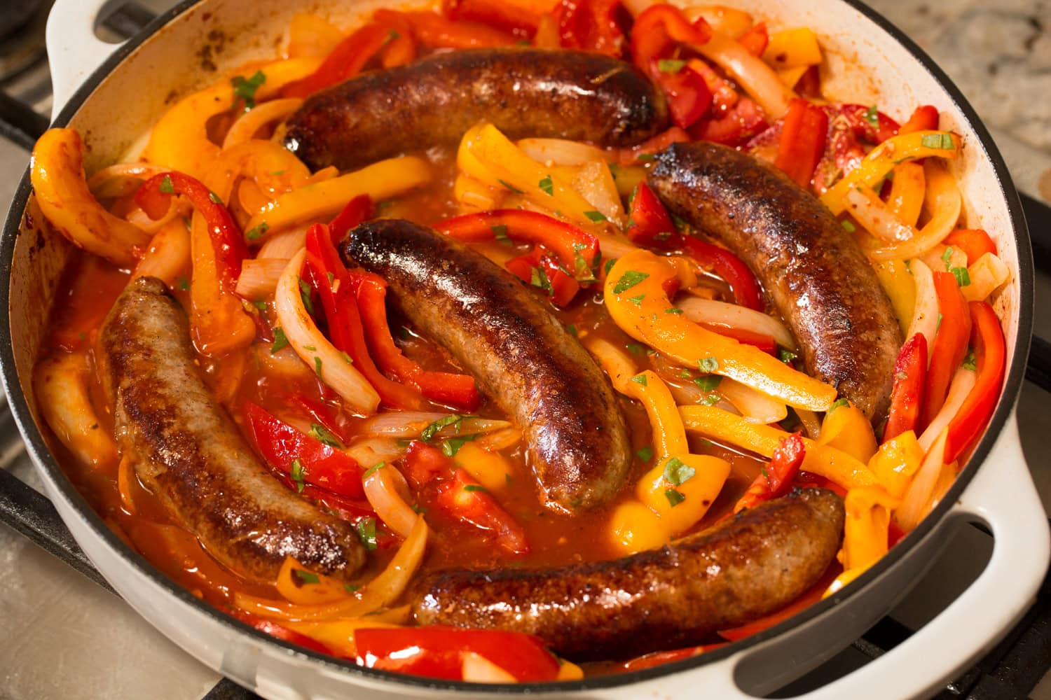 Italian Sausage Peppers and Onions Browned sausages shown nestled into pepper and onion mixture in pan.