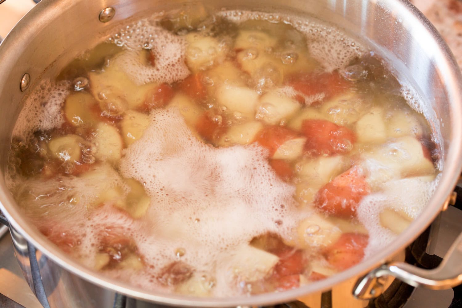 Red Potato Salad Chopped red potatoes being boiled on the stove in a pot.